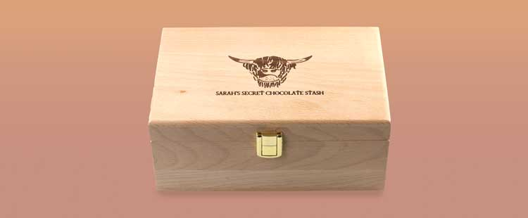 A wooden box with a gold latch, featuring an engraved animal head and the text SARAHS SECRET CHOCOLATE STASH on the lid, placed on a gradient background.