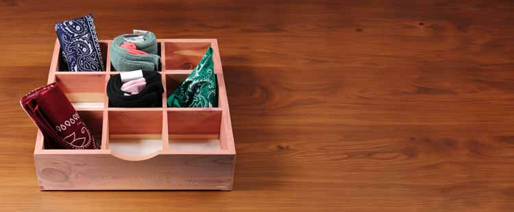 A wooden organizer box with nine sections, each containing neatly folded bandanas of various colors, sits on a wooden surface.