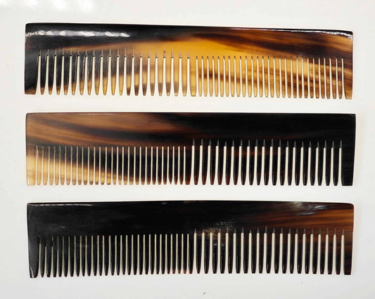 Lined up against a white background, three Cathcart Elliot 6-inch rectangular horn combs showcase their natural brown and black gradient. These pocket-sized grooming essentials feature fine, evenly spaced teeth for style and functionality.