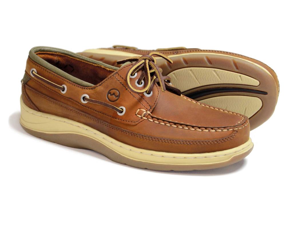 A pair of Orca Bay Squamish mens sand nubuck deck shoes features brown leather, beige non-marking rubber soles, and tan laces, with side lacing details and a small circular logo. One shoe stands upright while the other is slightly tilted to showcase the sole.