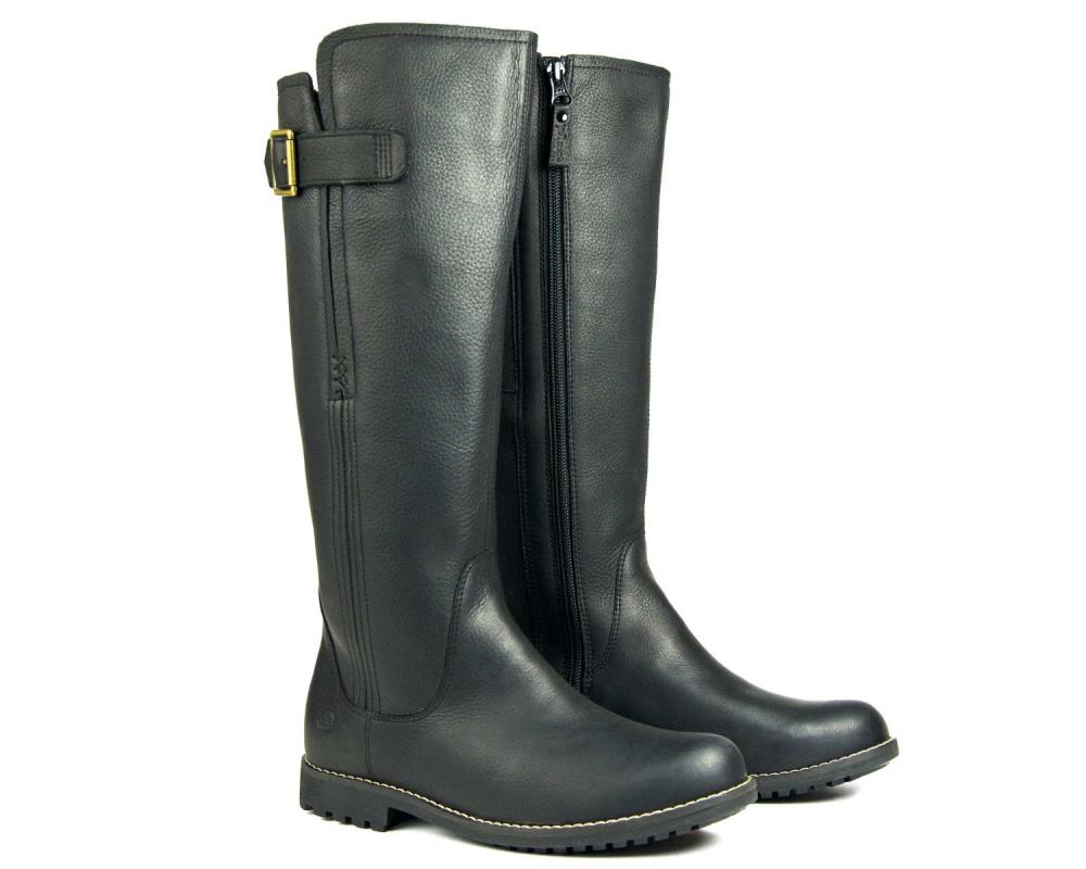The SALE Ladies Moreton Tall Boot in Black Leather by Orca Bay features cushioned footbeds, low heels, and side zippers. Decorative straps with buckles adorn the top, providing style and stability with textured soles for winter grip. Displayed upright against a white backdrop.