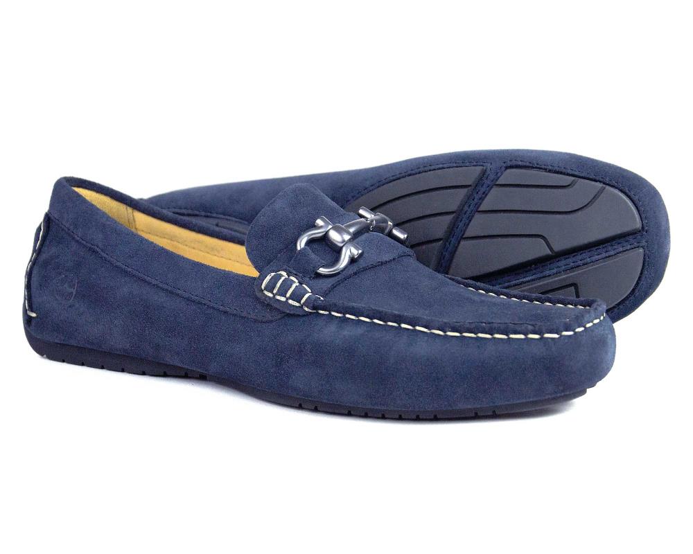 The Orca Bay ROMA 2 Mens Navy Suede Driving Loafers feature premium suede, white stitching, silver metal front detail, rubber soles, and tan leather lining. One shoe stands upright while the other displays the sole.