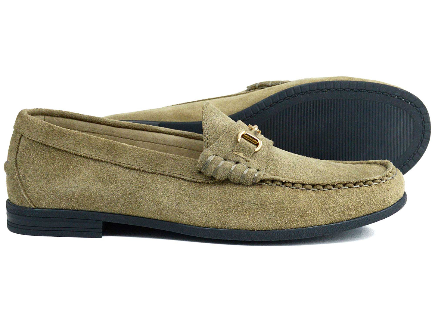 The Orca Bay Zurich Ladies Taupe Suede Buckle Loafer features moccasin-style stitching, black soles, and a small metal buckle on the side. One loafer stands upright while the other is tilted to showcase its sole.