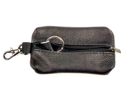 The Cathcart Elliot Black Grain Leather Key Wallet features a silver zip closure that partially reveals a metal keyring. A small silver clasp on the zipper allows for easy attachment. The textured leather adds elegance and versatility to the design.