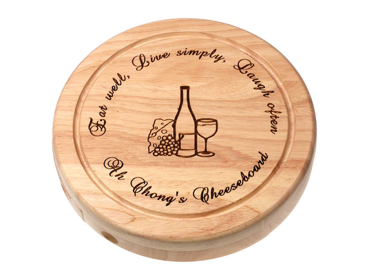 The Cathcart Elliot Personalisable 19cm Round Cheeseboard Gift Set features a wire cutter, tongs, and engraving of a wine bottle, glass, cheese, grapes, plus “Eat well, Live simply, Laugh often”—a thoughtful gift for cheese lovers.