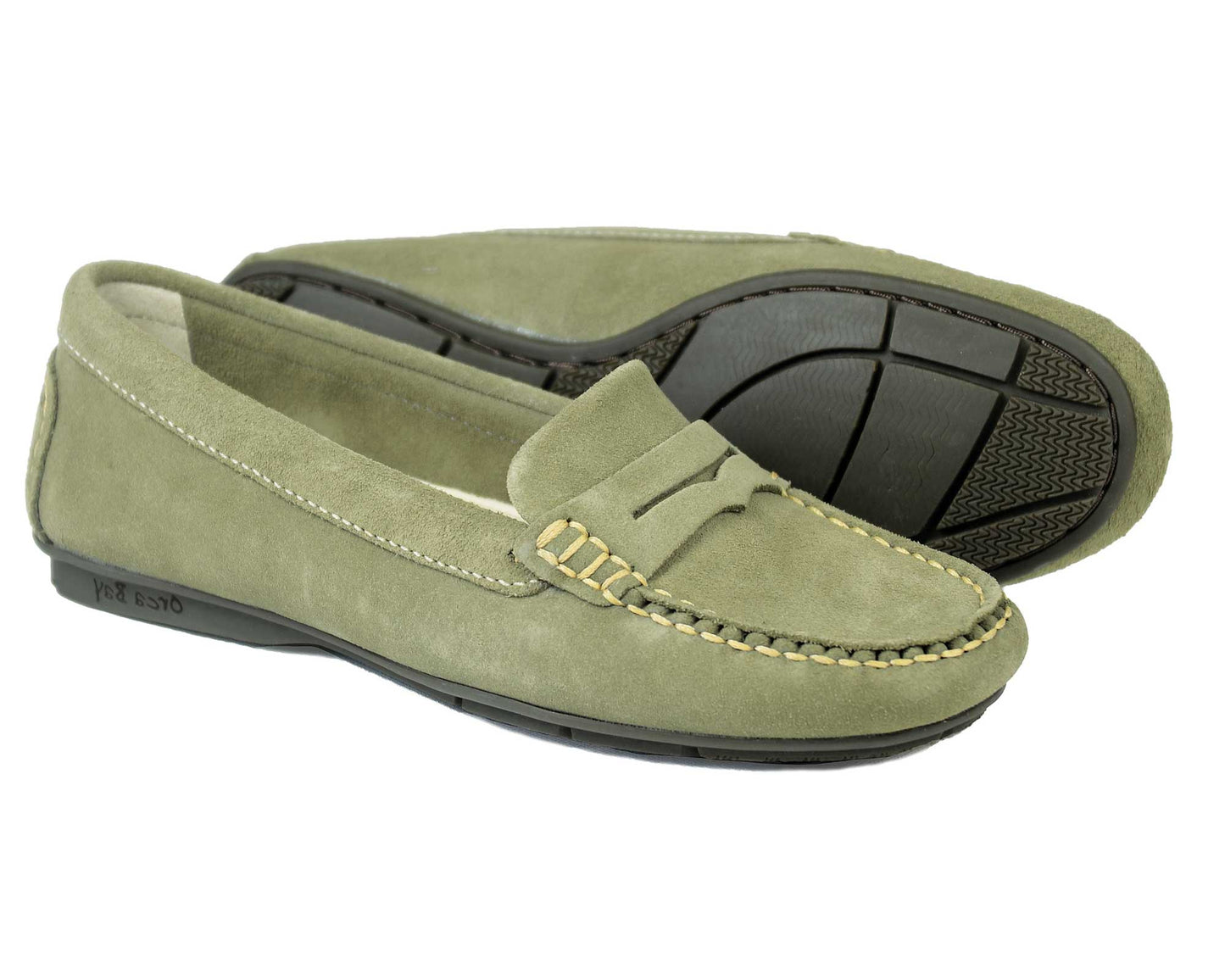 The FLORENCE Ladies Sage Suede Summer Loafer by Orca Bay features detailed edge stitching, a classic penny slot, and a comfortable black rubber sole. One shoe is displayed upright while the other is on its side.