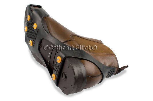 Cathcart Elliot Studded Ice Grippers attach to brown dress shoe soles, featuring black rubber with orange studs for secure traction on snow and ice—ideal winter aids for slippery surfaces.