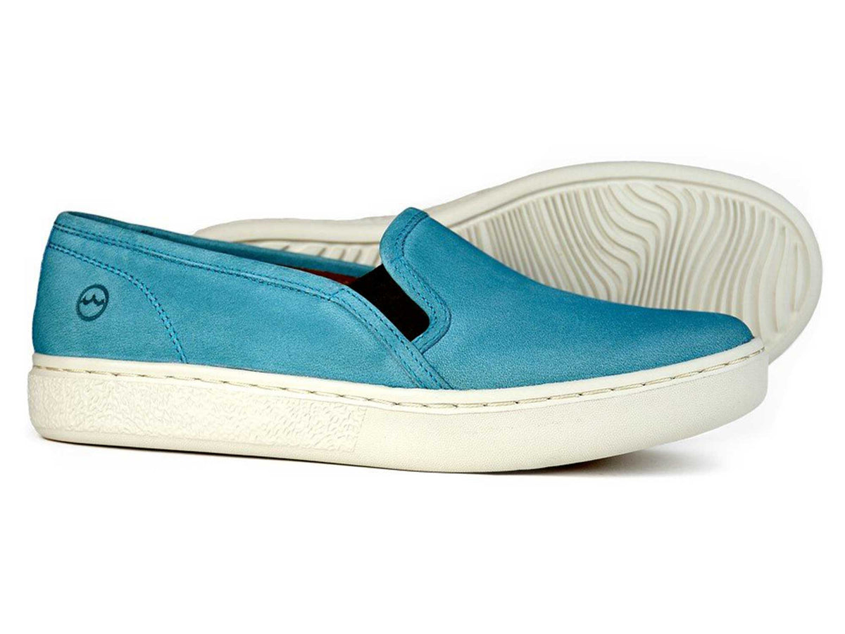 The MARYLEBONE Ladies Aqua Blue Summer Loafer by Orca Bay is a comfortable womens shoe made from nubuck leather, featuring white rubber soles—one shown upright and one on its side to highlight the textured sole.