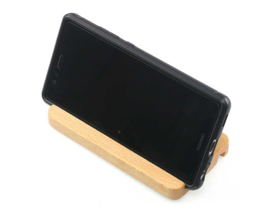 A black smartphone in a black case rests on a Cathcart Elliot beech wood phone stand against a white background.