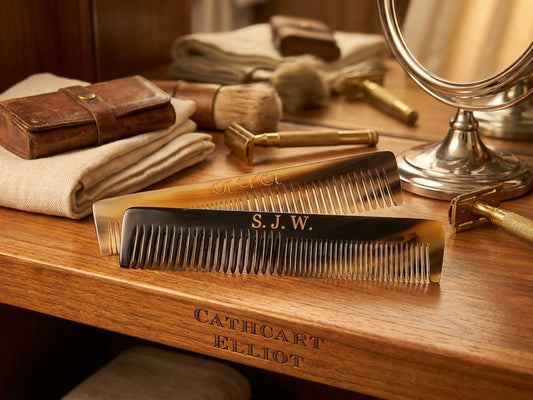 Two personalised 6-inch handmade real ox horn combs by Cathcart Elliot, one engraved with S.J.W., rest on a wooden vanity beside a mirror, towel, brushes, leather case, and have "Cathcart Elliot" elegantly engraved on the vanity.
