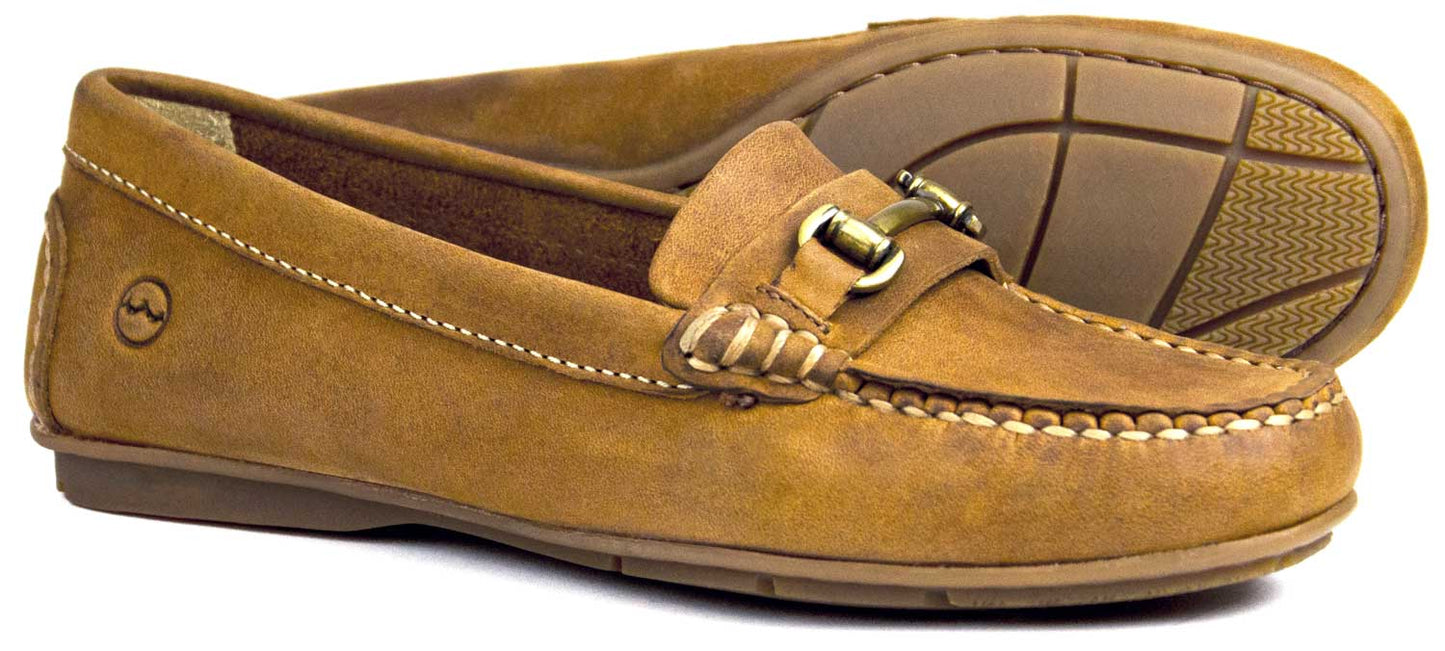 Orca Bay VERONA Ladies Loafers in sand nubuck feature stitching details and gold buckles. The non-slip sole ensures secure footing, while one shoe stands upright with the other leaning to reveal its comfy footbed and tread.