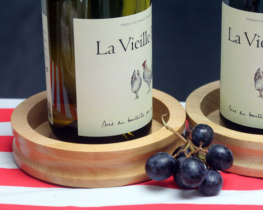 A close-up of two La Vieille wine bottles on Cathcart Elliot Personalised Wine Bottle Coasters made from beech wood, with black grapes beside one bottle, all arranged on a red and white striped surface.