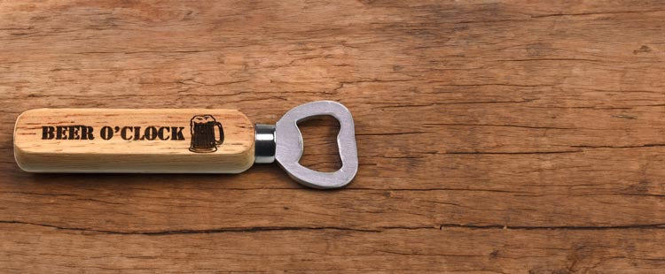 Wooden-handled bottle opener with BEER OCLOCK and a beer mug image etched on it, placed on a rustic wooden surface.