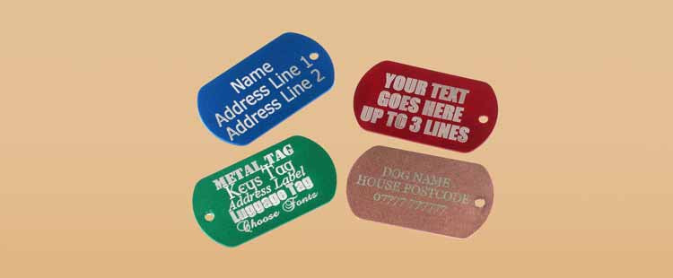 Four engraved dog tags on a beige background: blue, red, green, and bronze. Each tag displays lines of text, demonstrating customization options with placeholders for names, addresses, and other details.