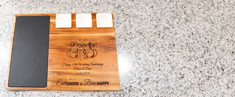 A wooden charcuterie board with a slate section and three ceramic dishes. Engraved with a romantic design and text: Happy 45th Wedding Anniversary Mom & Dad 16/9/1978, Eat Cheese & Brie Happy.