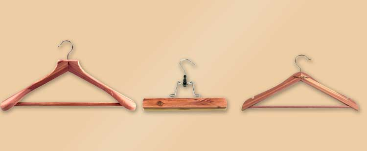 Three wooden hangers against a beige background: a suit hanger on the left, a clamp hanger in the middle, and a classic shirt hanger on the right.