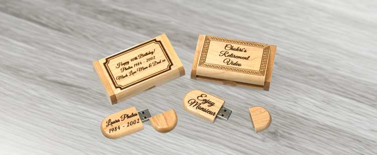 Go to the Wooden USB drives and boxes engraved with commemorative dates and names. One box reads Enjoy the memories, while the drives are labeled with names and significant years, resting on a light gray surface. collection