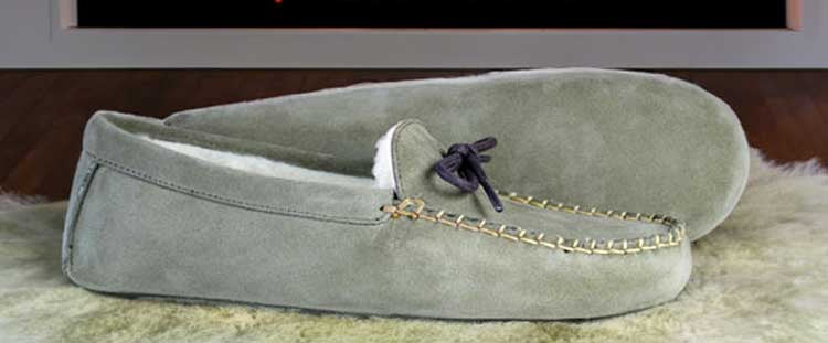 A pair of brown leather boat shoes with white stitching and laces, featuring rubber soles, placed on a plain beige background.