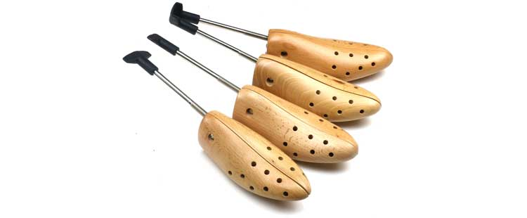 Four wooden shoe stretchers with metal rods and black handles are laid out on a white background. Each stretcher has multiple holes for breathability and adjustable width.