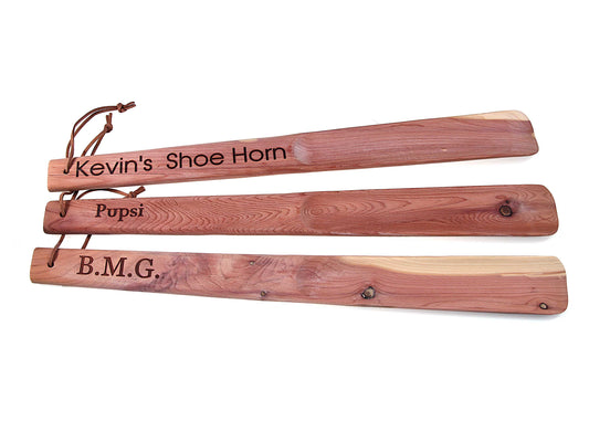 Three wooden shoe horns with engraved names on a white background