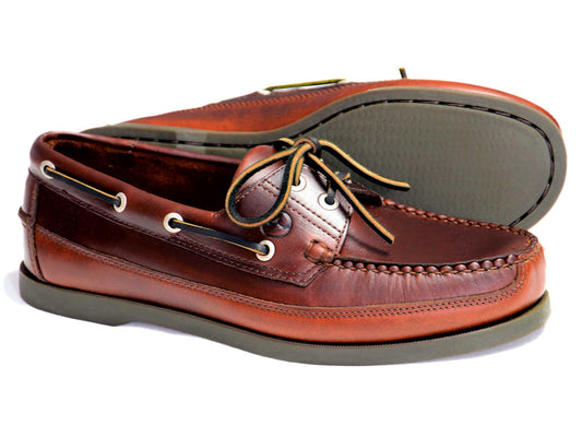 The AUGUSTA Mens Sailing Shoes 'Elk' Brown Leather by Orca Bay feature white stitching, tan laces, and thick rubber soles. One shoe stands upright while the other leans on its side to show the textured bottom.