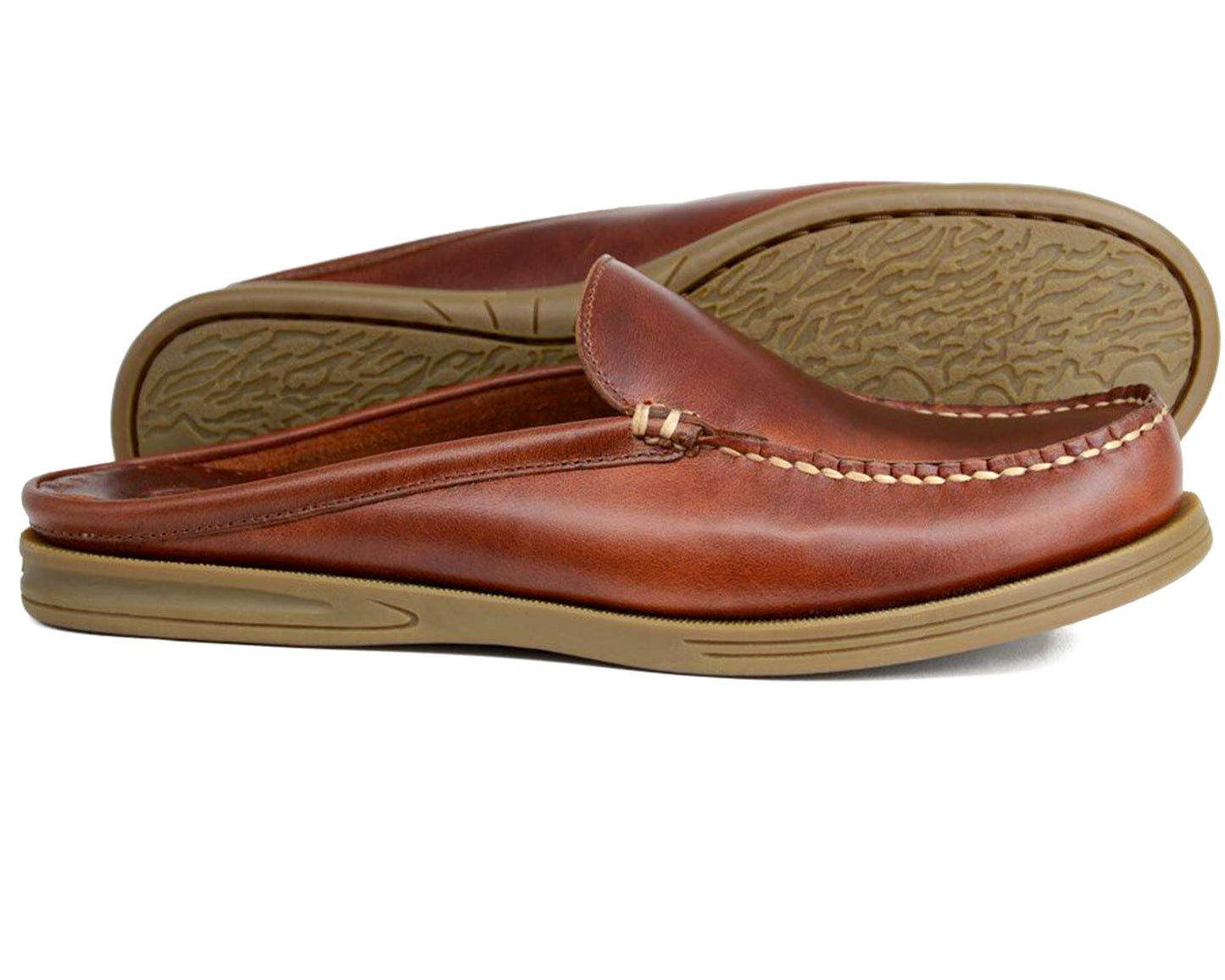 The Orca Bay BERWICK MULE Men's Mule in Saddle Leather features a brown leather upper and tan rubber soles—one shoe upright, the other on its side to reveal the textured sole.