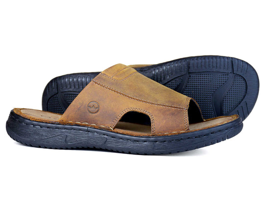 The Orca Bay BARBADOS Men’s Sandal features sand oiled nubuck leather and black rubber soles. One sits upright while the other lies on its side, showing the textured sole and cushioned footbed for comfort.