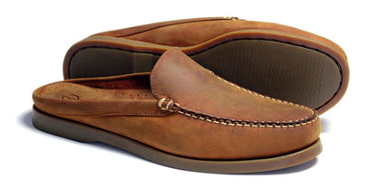 A pair of Orca Bay Mule Men’s Slip-On Deck Shoes in sand oiled nubuck, with classic stitching and flat rubber soles, one shoe lying on its side and the other standing upright.