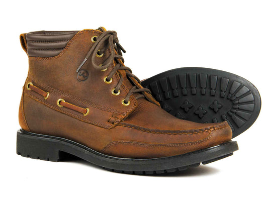The Orca Bay Dartmouth Men’s Leather Country Boot in Havana Brown features gold eyelets, brown laces, contrast stitching, and rugged waterproof soles. One boot stands upright while the other is angled to display its sturdy tread.