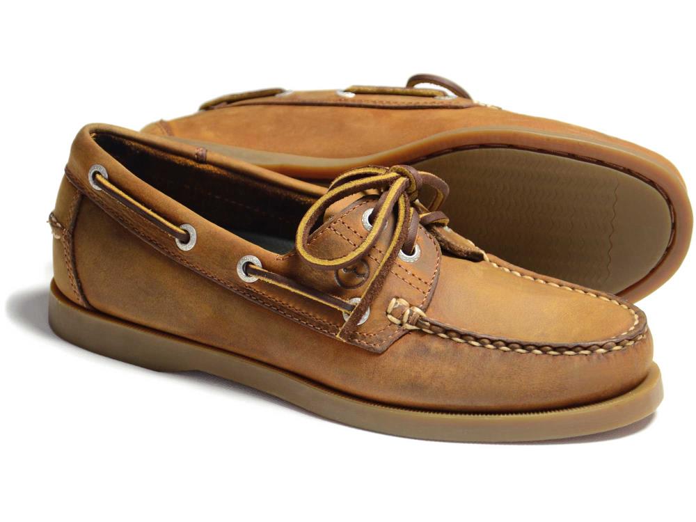 The CREEK Orca Bay Creek Ladies Deck Shoe in Sand features white stitching and laces, a smooth tan sole, slip-resistant design with two eyelets per side, and a classic moccasin style. One shoe is upright while the other is on its side.
