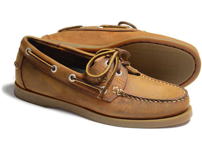 The CREEK Orca Bay Creek Ladies Deck Shoe in Sand features white stitching and laces, a smooth tan sole, slip-resistant design with two eyelets per side, and a classic moccasin style. One shoe is upright while the other is on its side.
