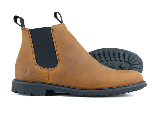 A pair of HENLEY Mens Ankle Boot – Sand Nubuck Chelsea Boots by Orca Bay, featuring black elastic side panels and black rubber soles; one stands upright while the other lays on its side to display the tread pattern.