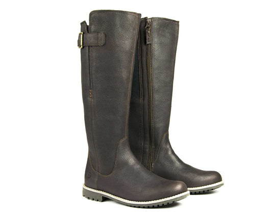 The Orca Bay Ladies Moreton Tall Boot in dark brown leather features side zippers, a decorative top buckle, and light-colored rubber soles. These chic winter boots stand upright side by side.
