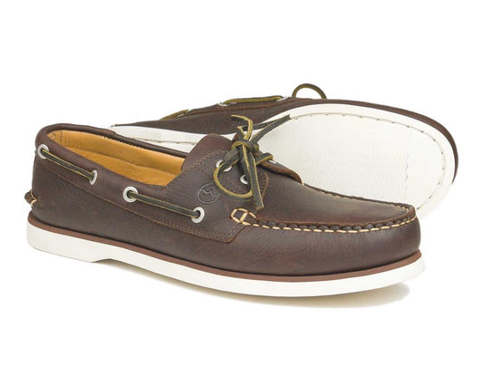 The PORTLAND Mens Dark Brown Nubuck Deck Shoes by Orca Bay feature a moccasin design with white soles, laces, and contrast stitching. One shoe stands upright while the other leans to showcase its smooth leather finish.