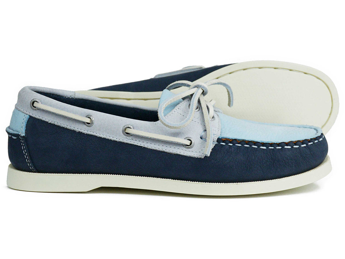 A pair of Orca Bay Ladies Sandusky Ice Indigo Luna Deck Shoes, featuring two-tone blue and light gray uppers with white non-marking soles, laces, and visible stitching; one shoe is pictured in a side view while the other is shown sole-up behind it.