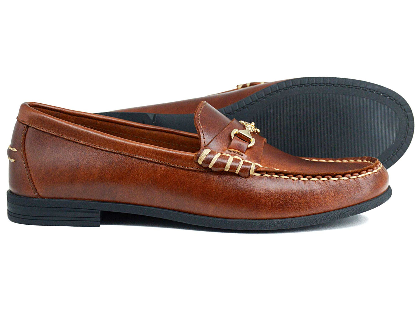 The Orca Bay Zurich Ladies Brown Saddle Leather Buckle Loafers feature gold buckles, stitching details, and black rubber soles. One shoe is shown in profile, the other displays the sole. Brand: Orca Bay.
