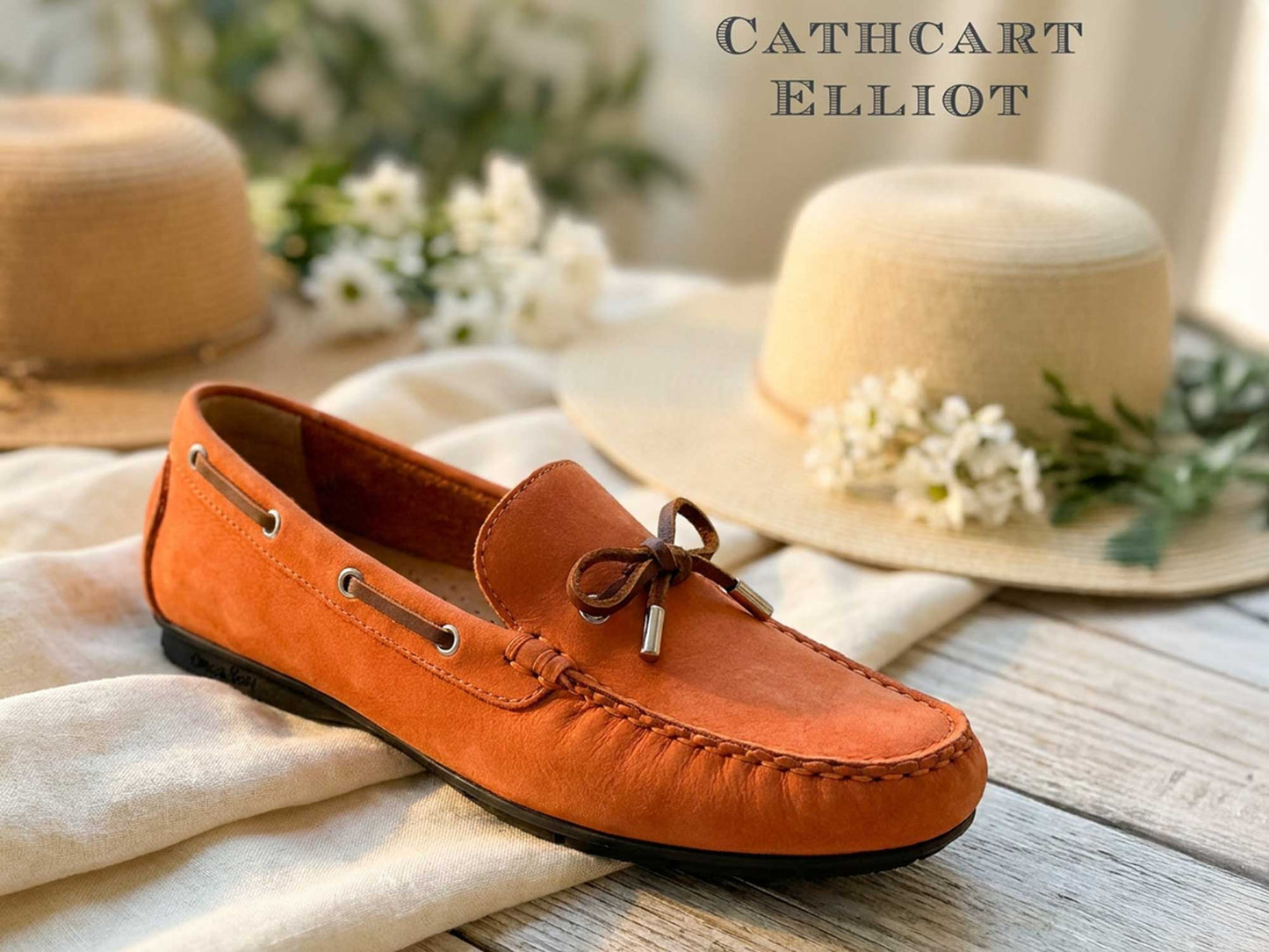 The Orca Bay Ballena Ladies Burnt Orange Loafers feature suede uppers and brown laces in a moccasin design, displayed on wood with light hats and white flowers behind. "Orca Bay" is shown in the top right corner.