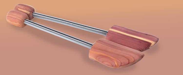 A pair of cedar shoe trees with metal springs, featuring smooth, polished wood on a gradient background of light to dark brown.