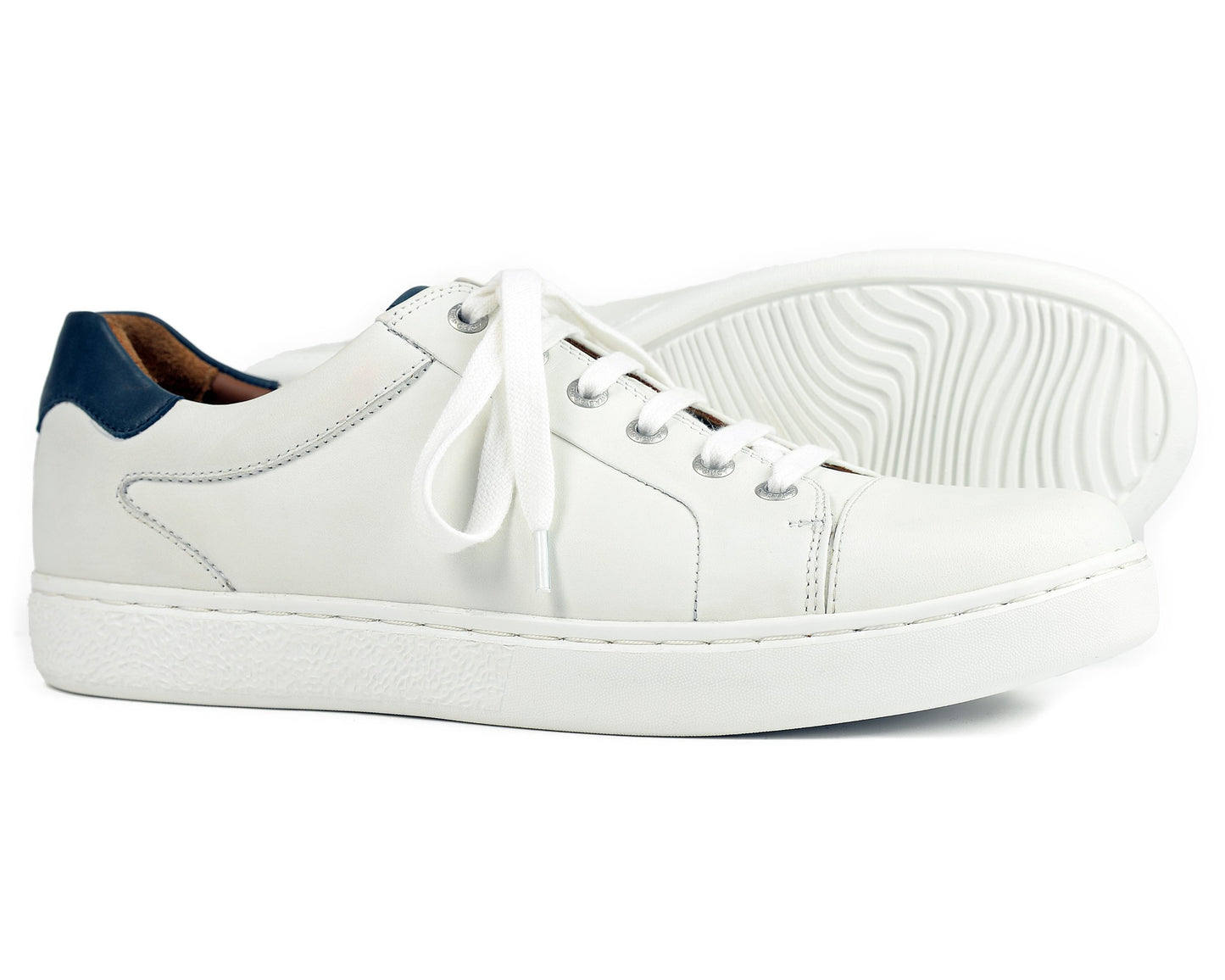 The BELGRAVIA Ladies White Sneaker by Orca Bay, a premium leather sneaker with a low-cut design, features white laces and a blue heel accent. Displayed on a white surface, one shoe upright and the other on its side showcase the shock-absorbing insoles and sole pattern.