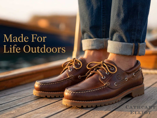A close-up of a person wearing BUFFALO ELK - Mens Deck Shoes by Orca Bay in brown leather with rolled-up jeans, standing on a wooden dock by the water. Text reads: Made For Life Outdoors and Orca Bay.