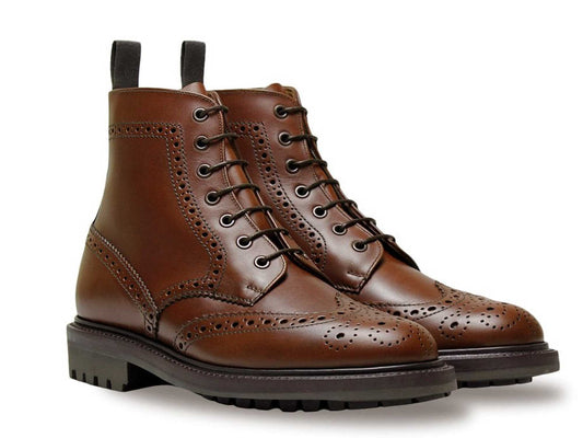 The CHELTENHAM Mens Brown Leather Brogue Boot by Sanders features intricate perforations, black laces, pull tabs at the back, and chunky Commando rubber soles. Displayed on a white background, these boots blend traditional style with rugged durability.