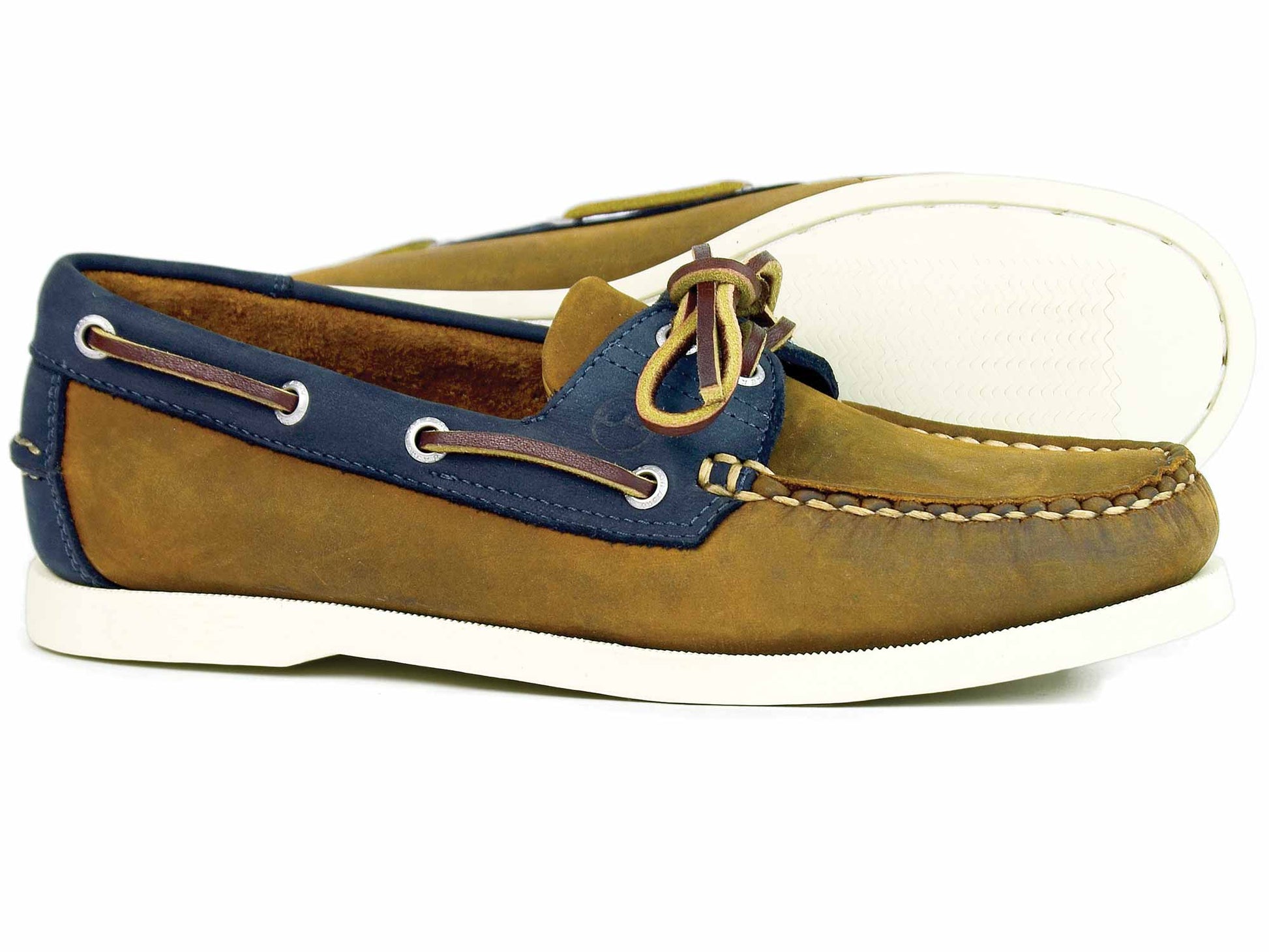 The CLOVELLY Ladies Sand Navy Nubuck Deck Shoe by Orca Bay is a pair of brown and navy leather boat shoes with moccasin construction, white soles, decorative side lacing, and a knotted lace on top, highlighting casual style and comfort.