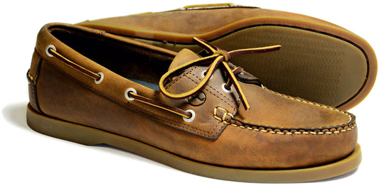The Orca Bay Creek Mens Deck Shoe in Sand is a pair of premium leather boat shoes featuring slip-resistant rubber soles, metal eyelets, laces, and white stitching for a casual look suitable for boating or everyday wear.
