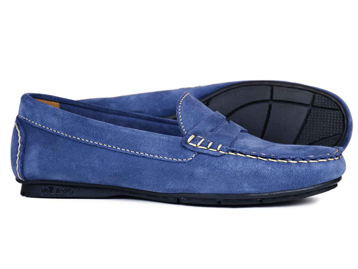 The FLORENCE Ladies Denim Blue Suede Summer Loafer by Orca Bay features white stitching, black rubber soles, and a classic slip-on design. One loafer is upright while the other is on its side, displaying the sole.