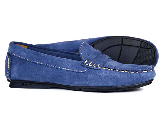 The FLORENCE Ladies Denim Blue Suede Summer Loafer by Orca Bay features white stitching, black rubber soles, and a classic slip-on design. One loafer is upright while the other is on its side, displaying the sole.