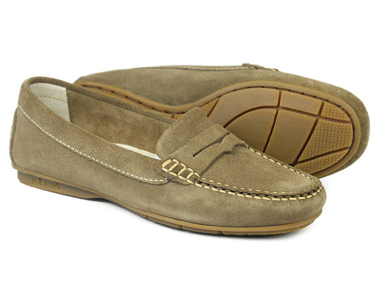 A pair of Orca Bay FLORENCE Ladies Mushroom Suede Summer Loafers, featuring stitching details and rubber soles. These classic loafers, crafted in mushroom suede, include a decorative strap on top. One shoe stands upright, while the other tilts to display its sole pattern.
