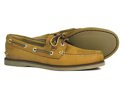 The NEWPORT Mens Premium Sand Nubuck Boat Shoes by Orca Bay feature a tan finish, brown laces, white stitching, and metal eyelets. One shoe is upright while the other tilts to showcase its sturdy rubber sole design.