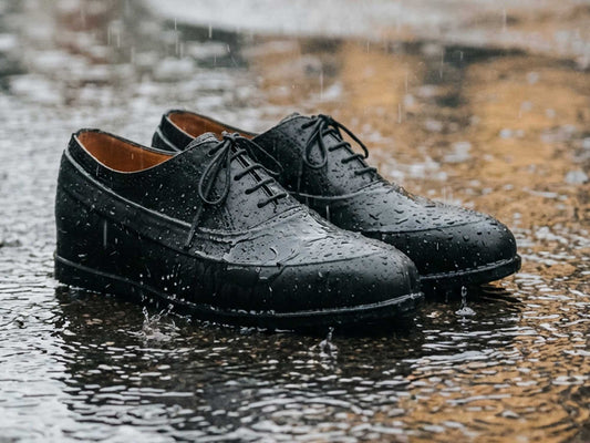 A pair of black leather dress shoes are splashed by rain—ideal for protecting with Cathcart Elliot’s Tough Rubber Galoshes, featuring a stretch fit and zigzag grip sole.