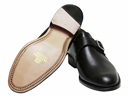 A pair of Sanders Rome Black Leather Monk Strap Shoes – Goodyear Welted: one displays the polished upper and side buckle, while the other is flipped to show its light tan sole with the Sanders logo stamped in gold.
