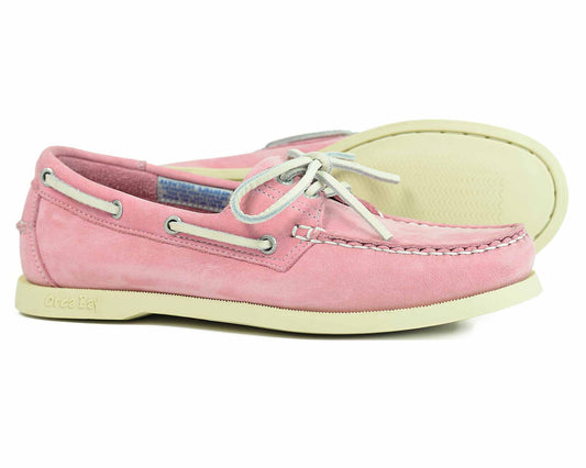 The Orca Bay SANDUSKY Ladies Boat Shoes in pink feature suede with white laces and eyelets. They come with a cream, non-slip rubber sole and display detailed toe stitching. One shoe is slightly tilted to highlight the tread pattern.